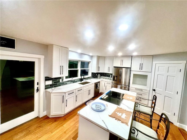 kitchen with appliances with stainless steel finishes, light wood-type flooring, light stone counters, sink, and white cabinets