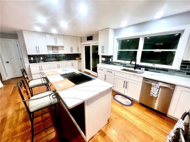 kitchen with stainless steel dishwasher, a kitchen island, white cabinets, and sink