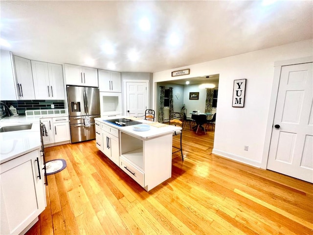 kitchen with stainless steel fridge, sink, light hardwood / wood-style flooring, white cabinets, and a center island