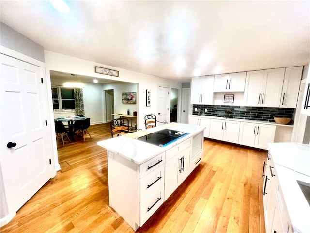 kitchen with a kitchen island, light wood-type flooring, white cabinetry, and black stovetop