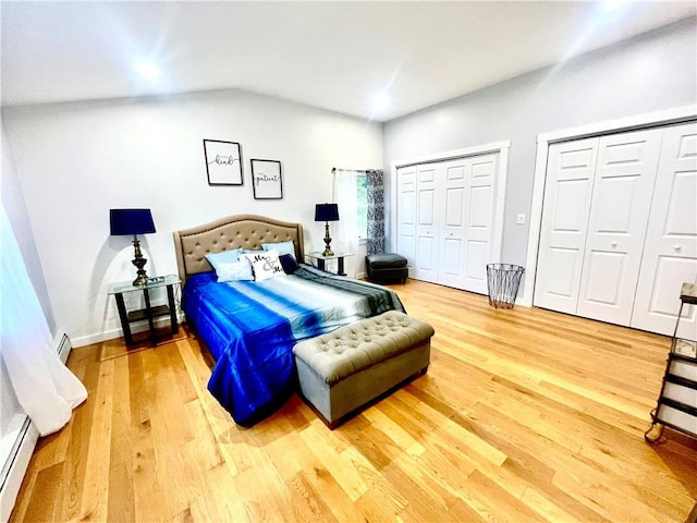 bedroom with vaulted ceiling, wood-type flooring, two closets, and a baseboard heating unit