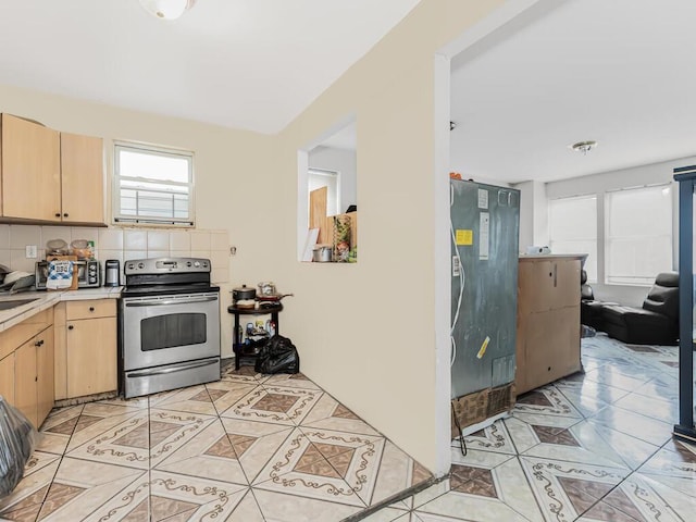 kitchen with light brown cabinets, backsplash, stainless steel electric range oven, light tile patterned floors, and fridge