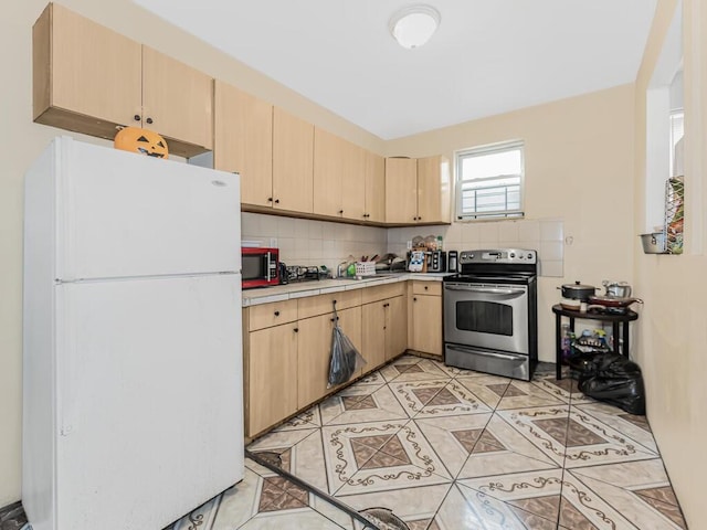 kitchen featuring light brown cabinets, stainless steel electric stove, decorative backsplash, light tile patterned floors, and white fridge