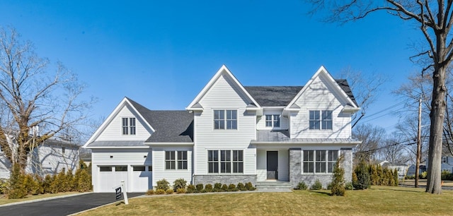 view of front of home featuring a front yard, a garage, stone siding, and driveway