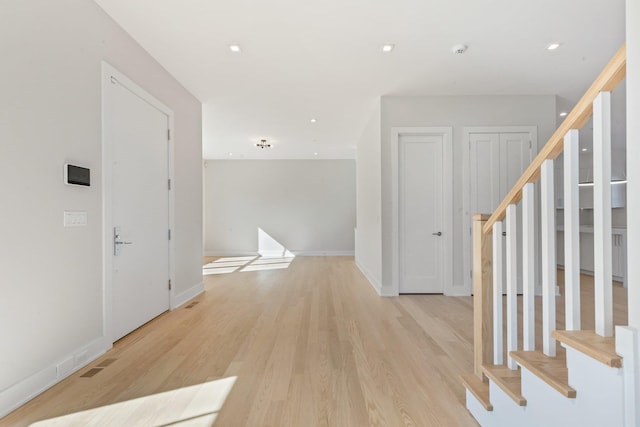 corridor with stairway, baseboards, visible vents, and light wood finished floors