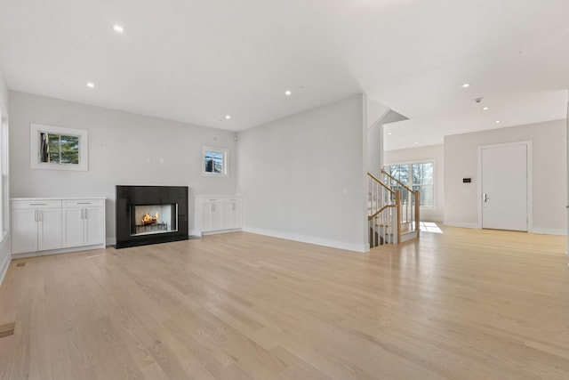 unfurnished living room with light wood-type flooring, recessed lighting, baseboards, stairway, and a multi sided fireplace