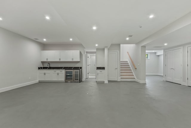 unfurnished living room featuring finished concrete flooring, recessed lighting, stairway, wine cooler, and baseboards