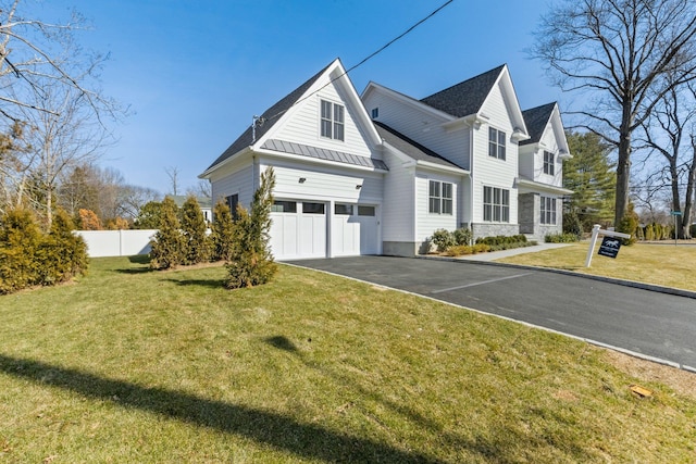 view of side of property with an attached garage, fence, a yard, driveway, and a standing seam roof