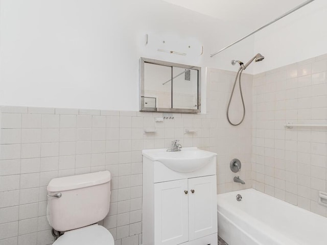 full bathroom with tiled shower / bath combo, toilet, tile walls, and vanity