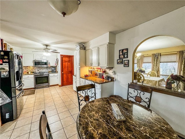 kitchen with appliances with stainless steel finishes, tasteful backsplash, ceiling fan, light tile patterned floors, and white cabinetry