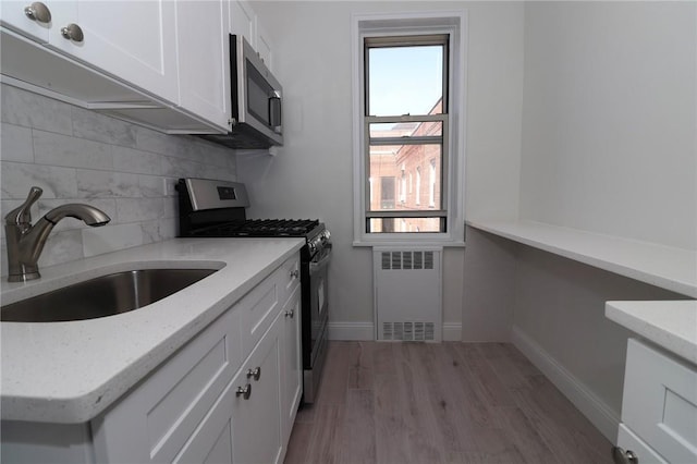 kitchen featuring radiator heating unit, sink, appliances with stainless steel finishes, light hardwood / wood-style floors, and white cabinetry