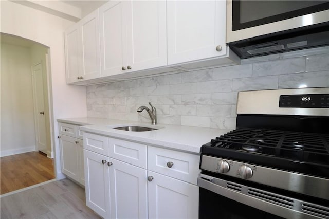 kitchen featuring white cabinetry, sink, light hardwood / wood-style floors, decorative backsplash, and appliances with stainless steel finishes