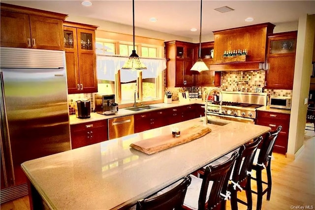 kitchen with pendant lighting, light hardwood / wood-style floors, high end appliances, and sink