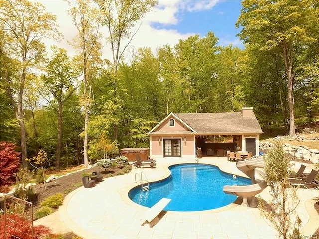 view of pool with a diving board, a hot tub, an outdoor structure, a water slide, and a patio