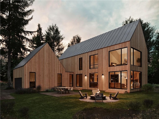 back house at dusk with a yard, a patio, and a fire pit