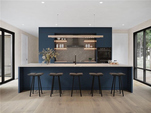 bar featuring black double oven, light hardwood / wood-style flooring, wall chimney exhaust hood, and sink