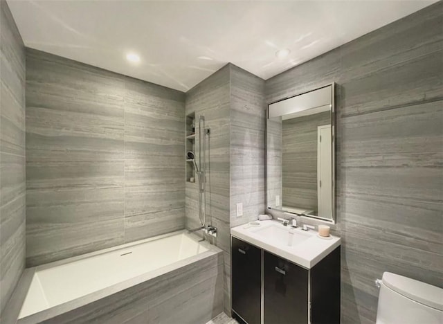 full bathroom featuring tiled shower / bath, vanity, tile walls, and toilet