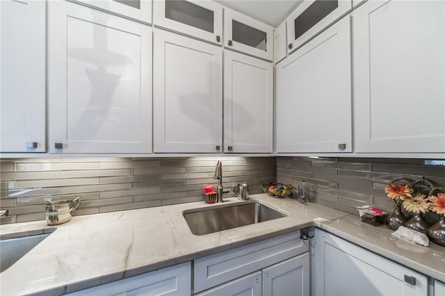 kitchen featuring tasteful backsplash, light stone counters, sink, and white cabinets