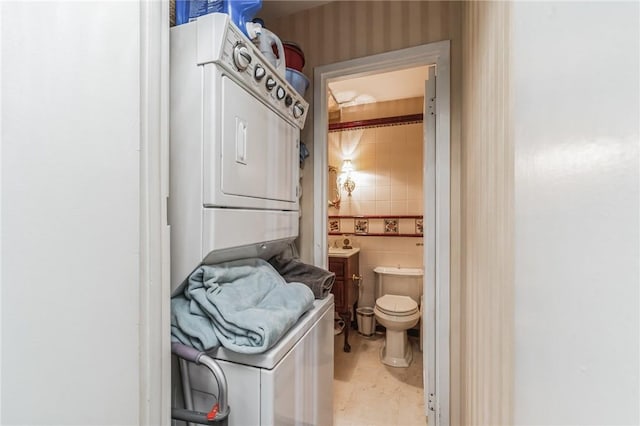 bathroom featuring stacked washer / drying machine, toilet, and tile walls