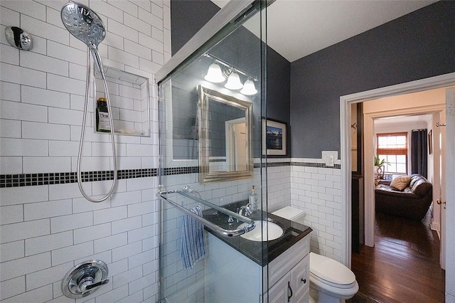 bathroom with hardwood / wood-style floors, vanity, toilet, tile walls, and a tile shower