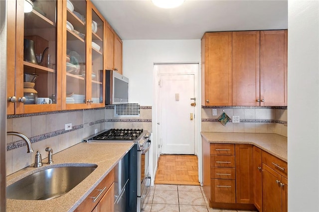 kitchen with appliances with stainless steel finishes, backsplash, light stone counters, light parquet floors, and sink