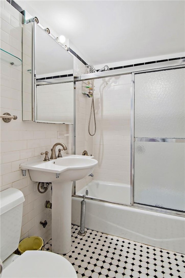 bathroom featuring toilet, tile walls, and bath / shower combo with glass door