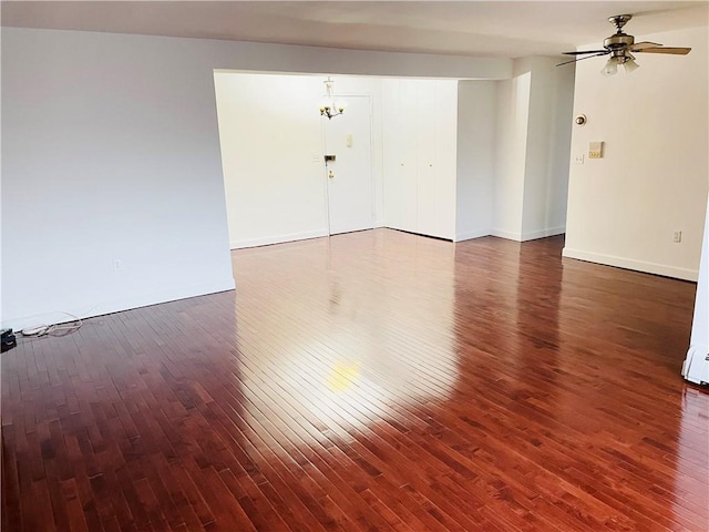 spare room with ceiling fan with notable chandelier and dark hardwood / wood-style flooring