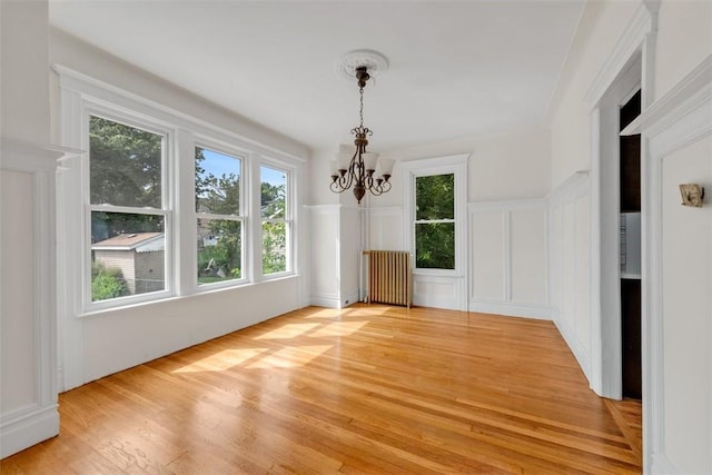 unfurnished dining area with radiator heating unit, light wood-type flooring, and an inviting chandelier