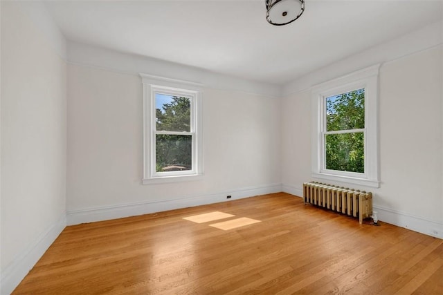 unfurnished room with radiator heating unit, plenty of natural light, and light wood-type flooring