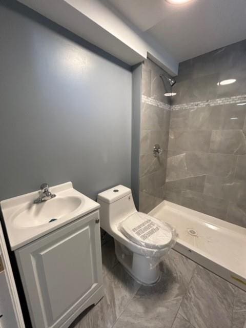 bathroom with tiled shower, vanity, and toilet