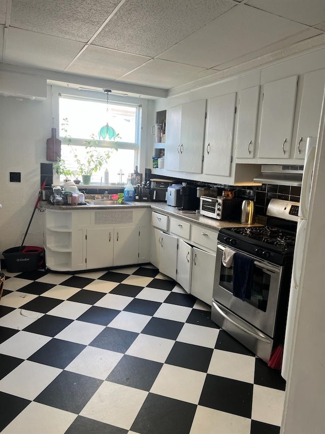 kitchen featuring a drop ceiling, decorative backsplash, stainless steel gas stove, and white cabinets