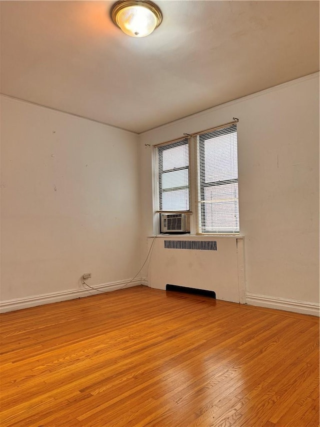 unfurnished room with radiator heating unit, cooling unit, and light hardwood / wood-style floors