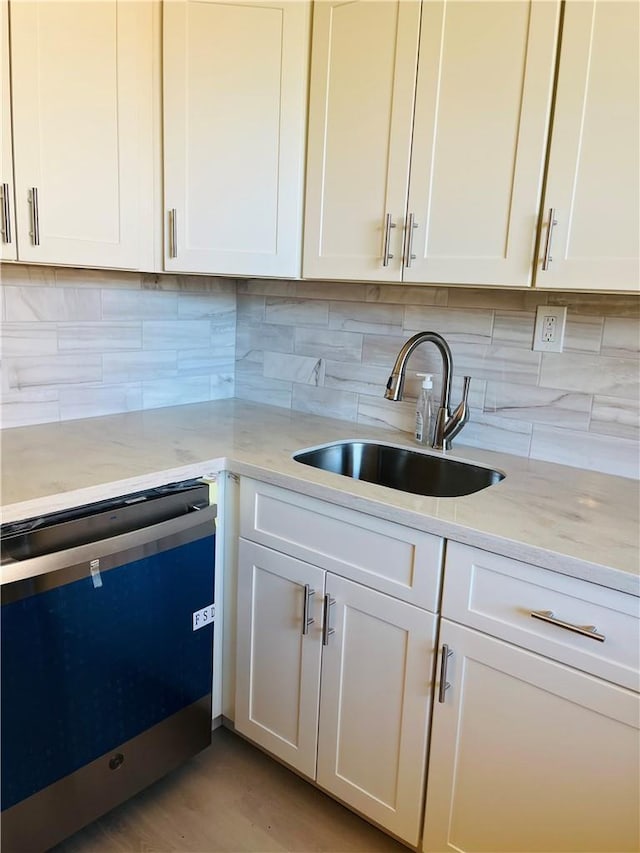 kitchen featuring light stone countertops, sink, tasteful backsplash, stainless steel dishwasher, and white cabinets