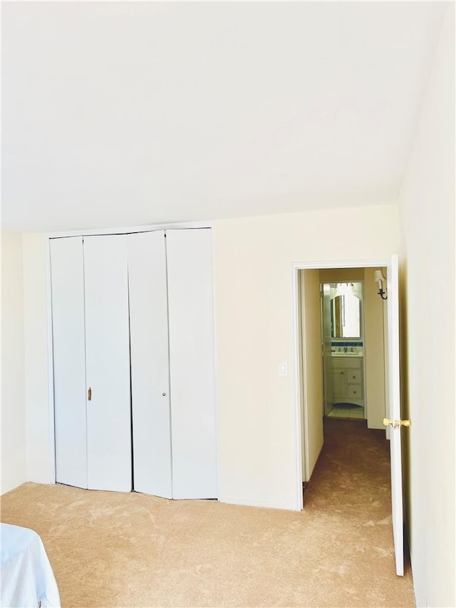 unfurnished bedroom featuring ensuite bath, light colored carpet, and a closet