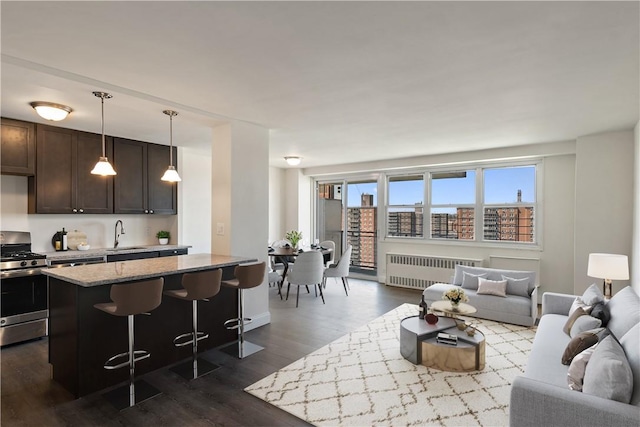 kitchen with radiator, light stone counters, dark hardwood / wood-style flooring, pendant lighting, and stainless steel stove