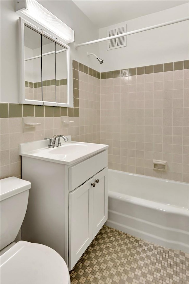 full bathroom featuring toilet, vanity, tiled shower / bath combo, and tile walls