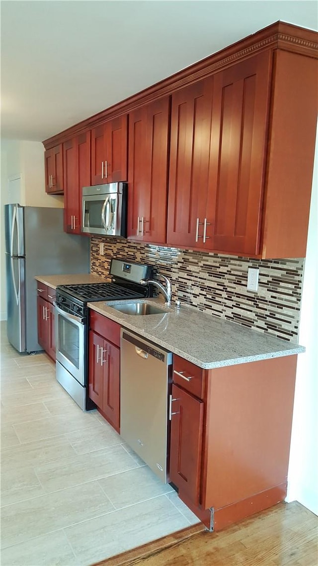 kitchen featuring tasteful backsplash, light stone counters, sink, and appliances with stainless steel finishes