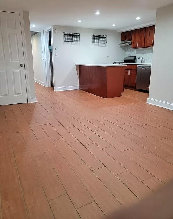 kitchen with stainless steel dishwasher, decorative backsplash, light wood-type flooring, and kitchen peninsula