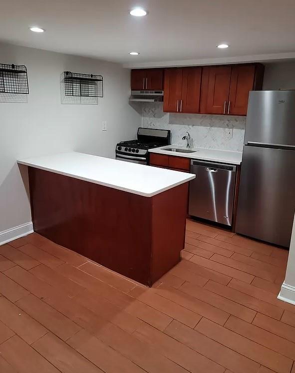 kitchen featuring sink, decorative backsplash, light hardwood / wood-style floors, kitchen peninsula, and stainless steel appliances