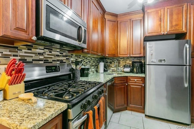 kitchen with light stone countertops, sink, decorative backsplash, light tile patterned floors, and appliances with stainless steel finishes