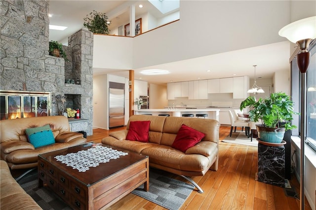 living room featuring a notable chandelier, light hardwood / wood-style floors, a towering ceiling, and a fireplace