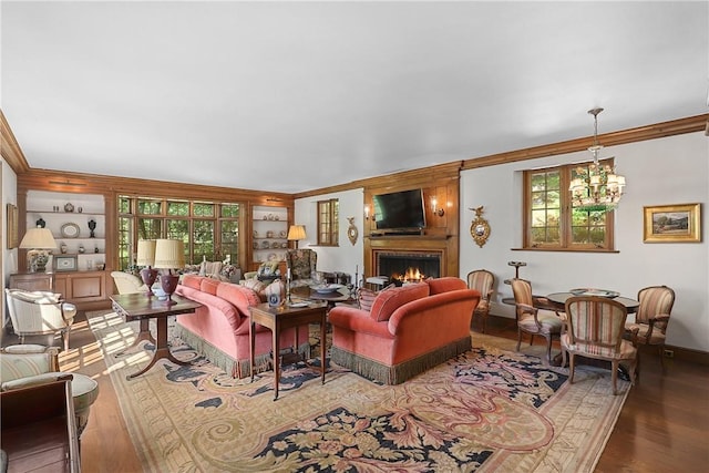 living room with crown molding, hardwood / wood-style flooring, an inviting chandelier, built in features, and a fireplace