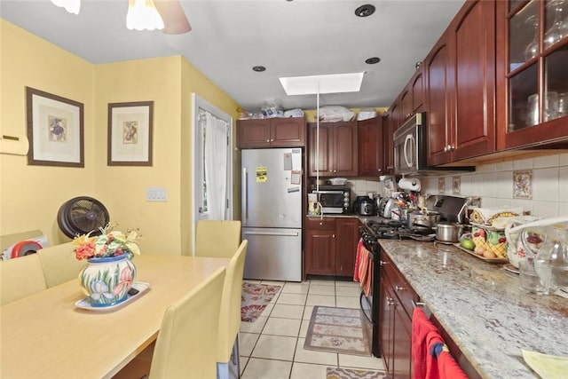 kitchen featuring a skylight, tasteful backsplash, light stone counters, light tile patterned floors, and appliances with stainless steel finishes