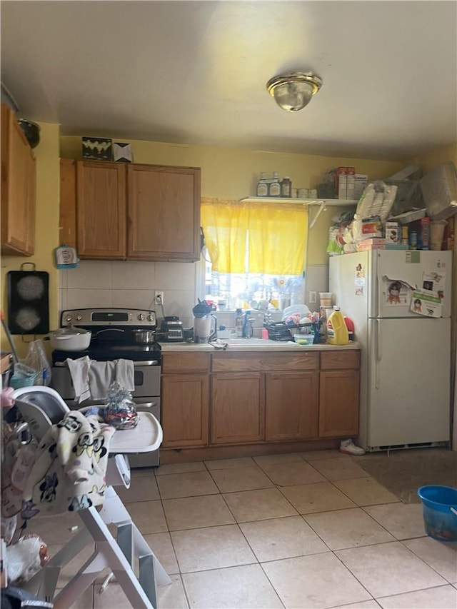 kitchen featuring decorative backsplash, white refrigerator, stainless steel range with electric stovetop, and light tile patterned flooring