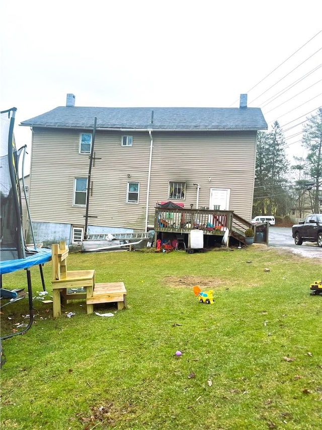 rear view of property with a lawn, a deck, and a trampoline