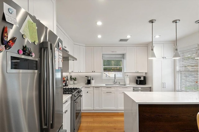 kitchen featuring stainless steel appliances, sink, pendant lighting, light hardwood / wood-style floors, and white cabinetry