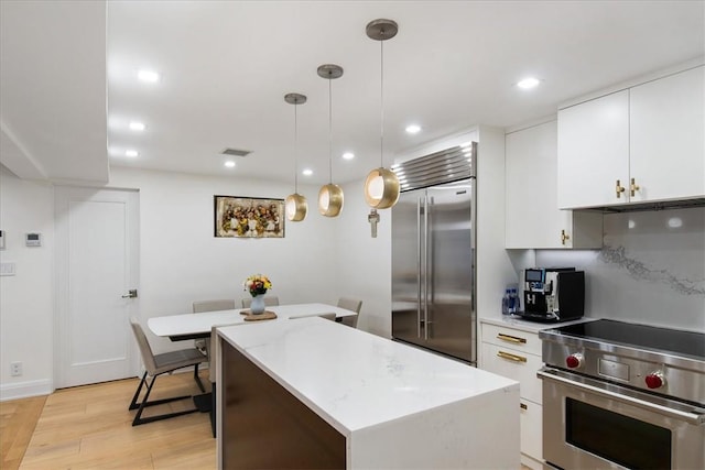 kitchen with white cabinetry, light hardwood / wood-style flooring, hanging light fixtures, and high end appliances