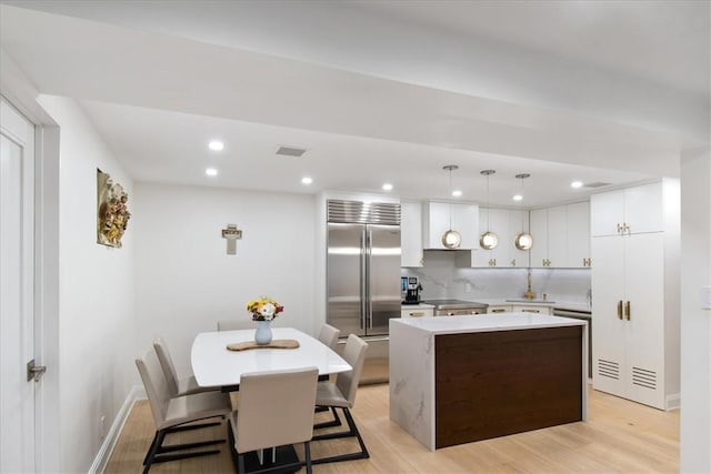 kitchen featuring pendant lighting, a kitchen island, stainless steel built in fridge, and light hardwood / wood-style floors