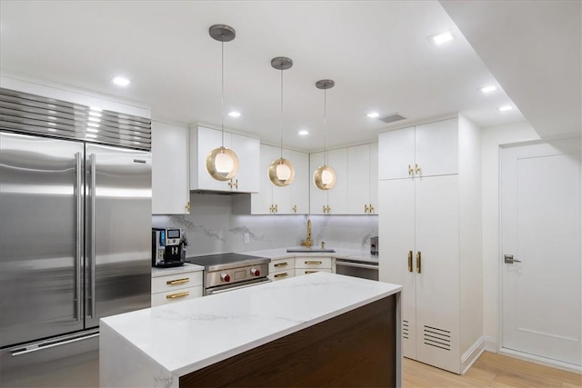 kitchen featuring light wood-type flooring, stainless steel appliances, pendant lighting, white cabinets, and a kitchen island