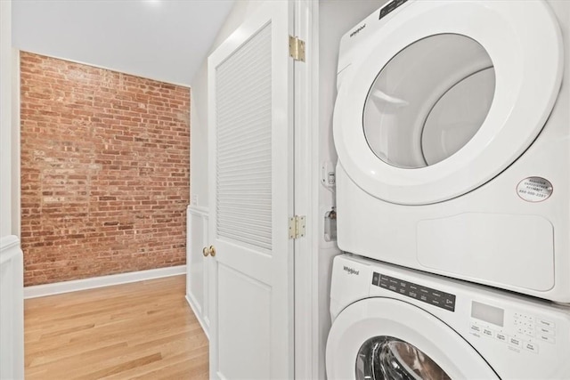 laundry area with brick wall, stacked washer / drying machine, and light hardwood / wood-style flooring